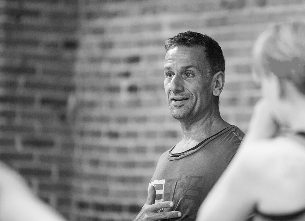 A black and white photo of a man speaking to a small group in front of a brick wall