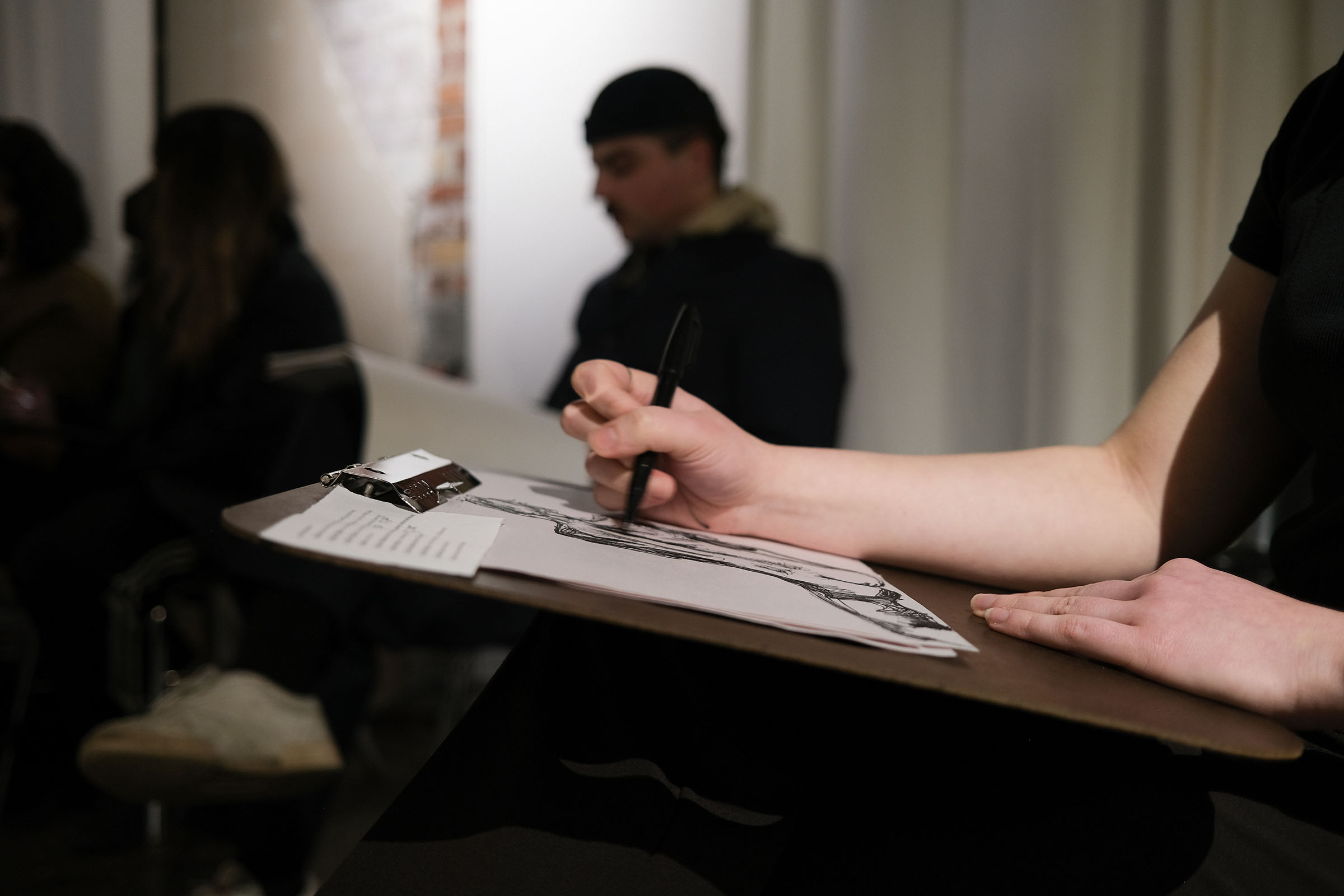 A photo of a persons hand sketching on a piece of paper on a clipboard